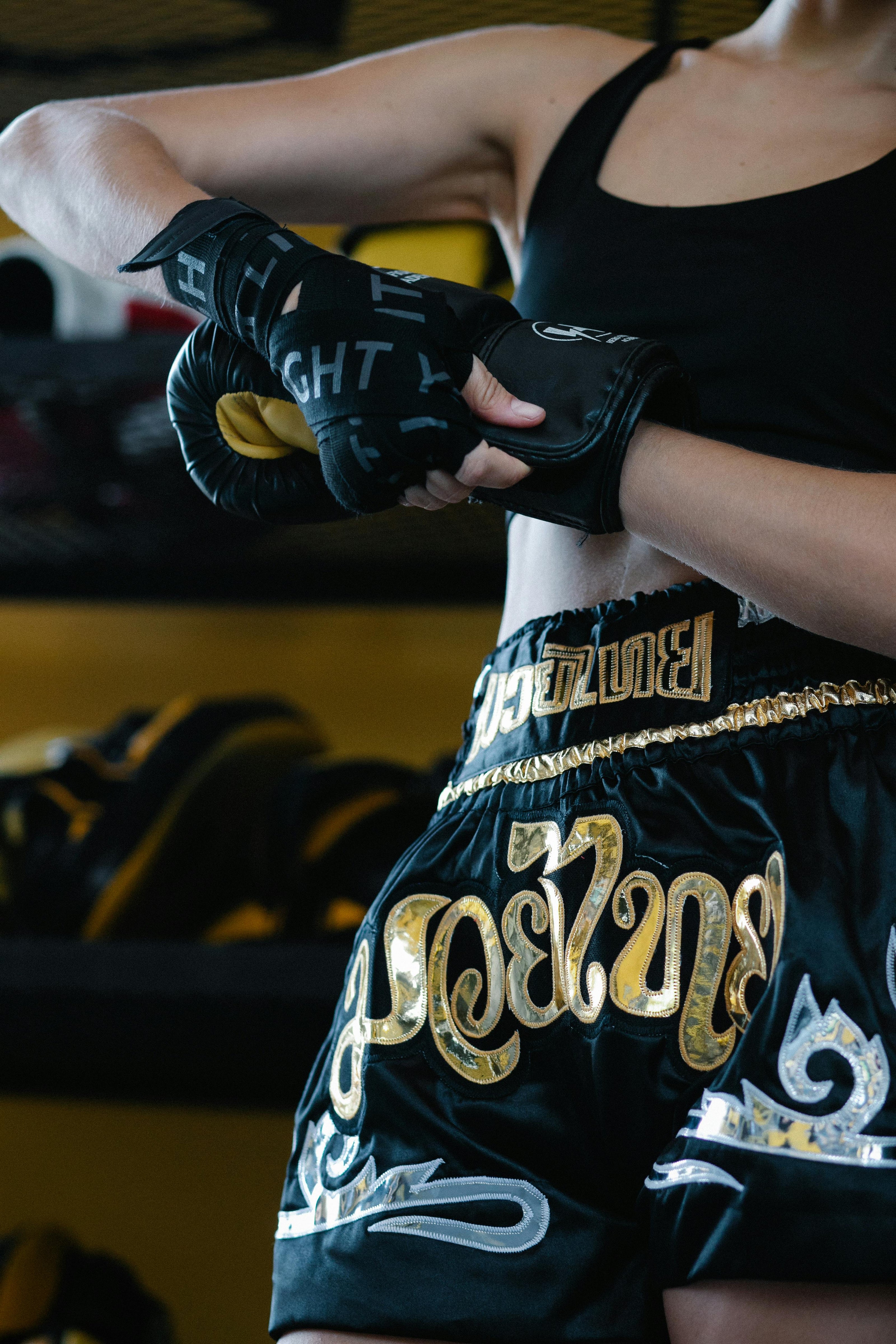 Person wearing black boxing gloves and green shorts with gold text in a gym setting