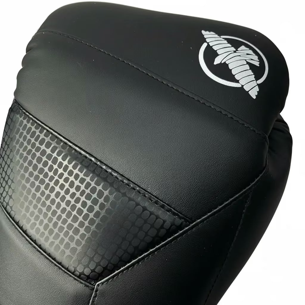 Close-up of a black boxing glove featuring a white stylized winged logo on the upper cuff and a textured honeycomb-patterned panel on the side, set against a plain white background.