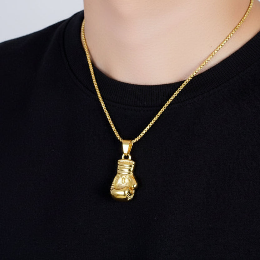 Gold boxing glove pendant on a necklace held by a person wearing a black shirt.