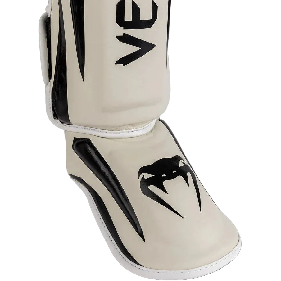 Beige shin guard with black logo on a gray background