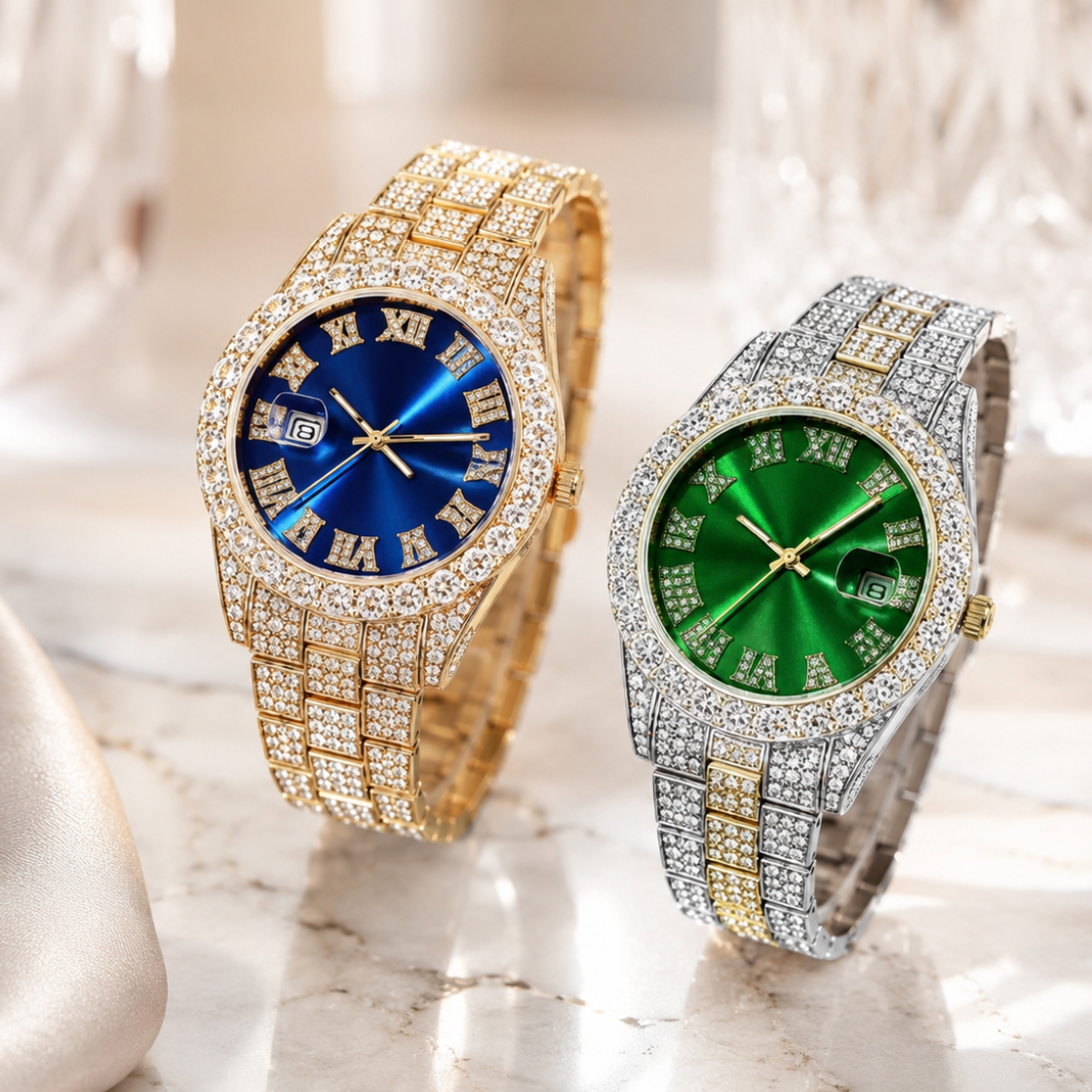 Two luxury wristwatches with diamond-encrusted metal bands and Roman numeral dials, one gold-tone with a blue dial and one silver-tone with a green dial, displayed on a marble surface with a blurred glass background.