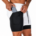 A close-up of a person wearing white and black athletic shorts, pulling a gray smartphone out of the side pocket of the shorts against a plain white background.