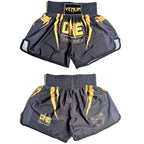 Two pairs of Venum fight shorts shown against a plain white background, one pair folded to show the front and one pair laid flat. The shorts are black with yellow graphics and logos, including 'Venum' on the waistband and 'ONE Championship' on the front.