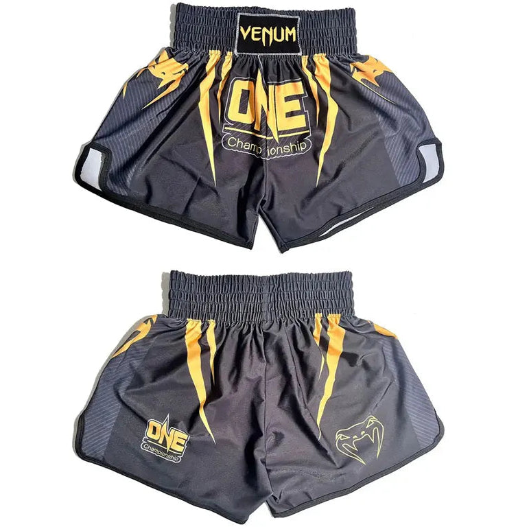 Two pairs of Venum fight shorts shown against a plain white background, one pair folded to show the front and one pair laid flat. The shorts are black with yellow graphics and logos, including 'Venum' on the waistband and 'ONE Championship' on the front.