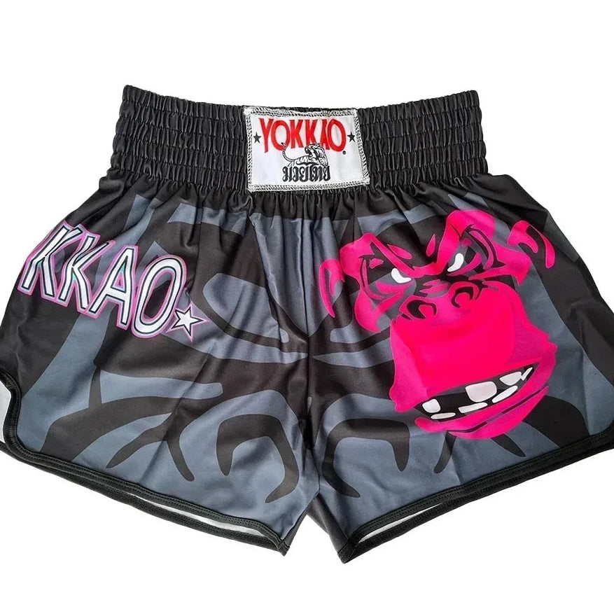 A pair of Yokkio Muay Thai shorts featuring a gray and black camouflage pattern with a large hot pink gorilla face graphic on the right leg and 'KKAO' text on the left leg.