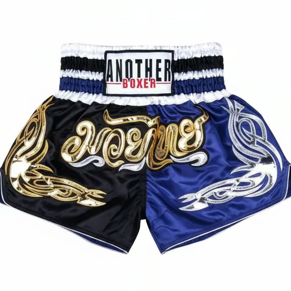 A pair of Muay Thai shorts by Another Boxer, featuring a split design with a black left leg and a royal blue right leg. The left leg is decorated with gold Thai script spelling 'Mae' and gold tribal patterns, while the right leg has a silver tribal pattern.