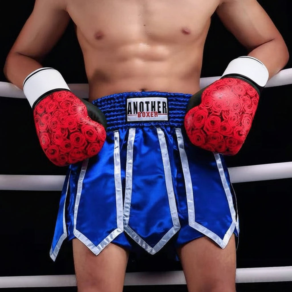 A cropped male boxer standing in a ring wearing blue satin trunks with white trim, red boxing gloves with a red rose pattern, and a visible ANOTHER BOXER waistband. The image includes ANOTHER BOXER branding and a store number watermark.