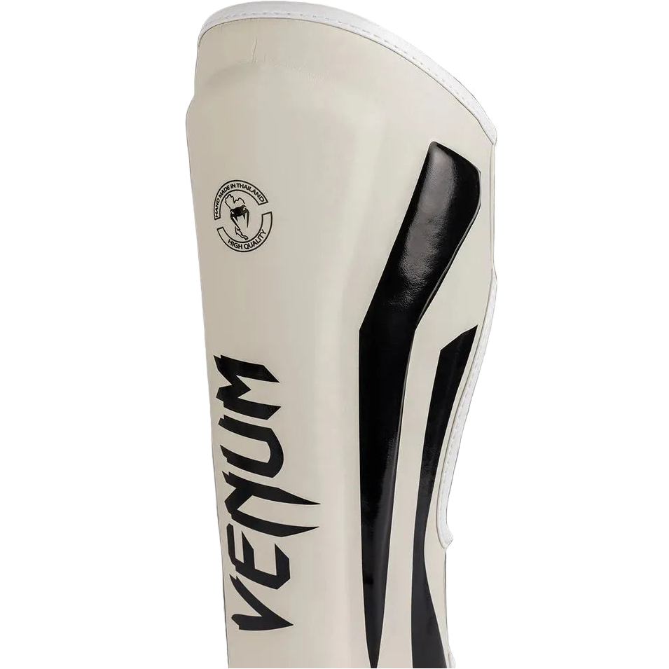 Beige shin guard with black accents and Venum logo on a gray background