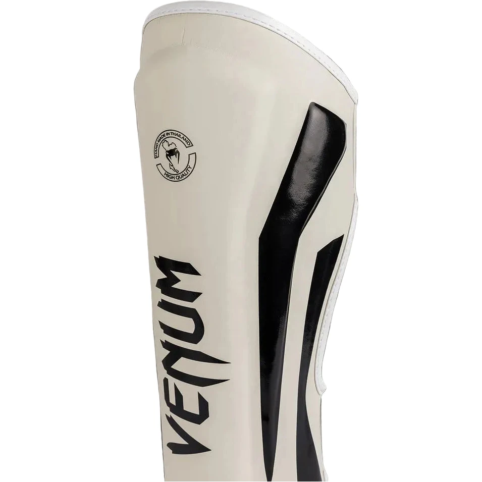 Beige shin guard with black accents and Venum logo on a gray background