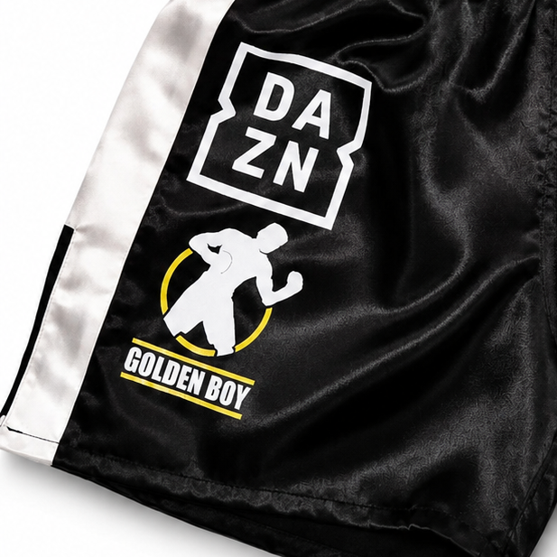 Black and white boxing shorts with multiple brand patches, including DAZN, WBC, Golden Boy, and Everlast, on a white background.