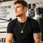Man in a black t-shirt with a gold necklace in a boxing gym.