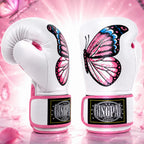 A pair of white boxing gloves with large pink, black, and blue butterfly designs on the back, featuring pink trim and a visible GINGPAI brand patch on the wrist area, set against a pink glittery background.