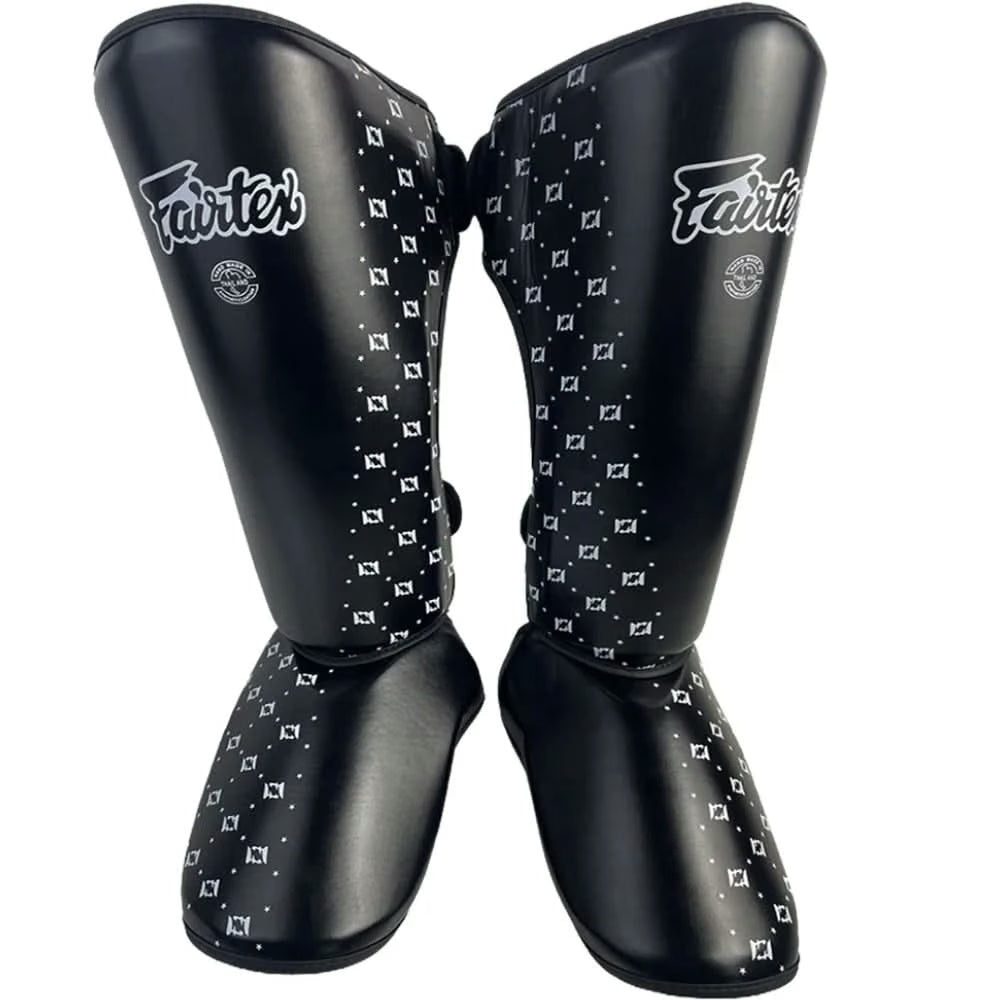 A pair of black Fairtex shin guards with white geometric patterns and white Fairtex branding, shown against a plain white background.