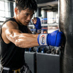 Boxer in training with blue boxing gloves hitting a punching bag in a gym.