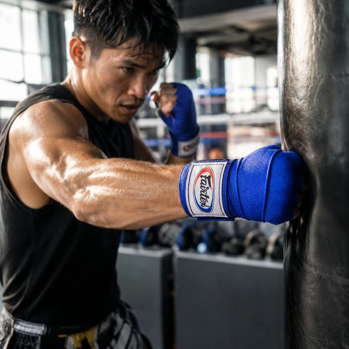 Boxer in training with blue boxing gloves hitting a punching bag in a gym.