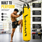 Man kicking a yellow punching bag with Fai'tex branding in a gym setting.