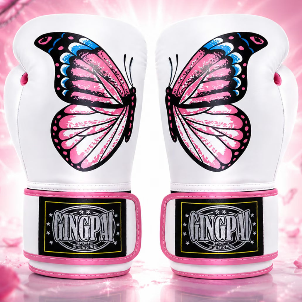 A pair of white boxing gloves featuring large pink, black, and blue butterfly designs on the front, with pink trim and a black GINGPA brand patch on the wrist straps, set against a pink sparkling background.