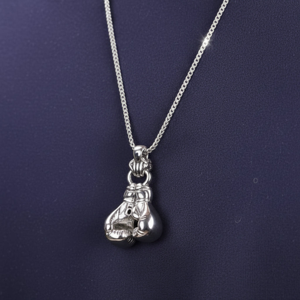 Silver boxing glove pendant necklace on a person wearing a dark blue shirt.