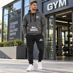 A man wearing a grey Lonsdale hoodie and black joggers stands outside a gym, with the Lonsdale logo visible on the hoodie and jogger thigh.