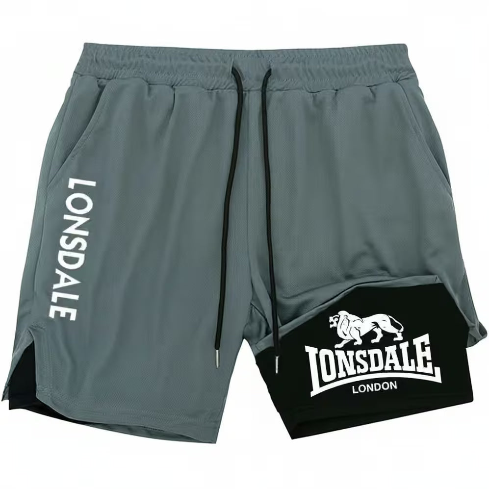 Lonsdale athletic shorts in a muted gray color, featuring a black drawstring, a vertical white 'LONSDALE' logo on the left leg, and a black patch with a white lion logo and 'LONSDALE LONDON' text on the right leg.