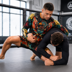 Two men in a gym, one wearing a colorful long-sleeve rash guard with a large bird graphic and matching shorts, while the other wears a black long-sleeve rash guard on a grappling mat.