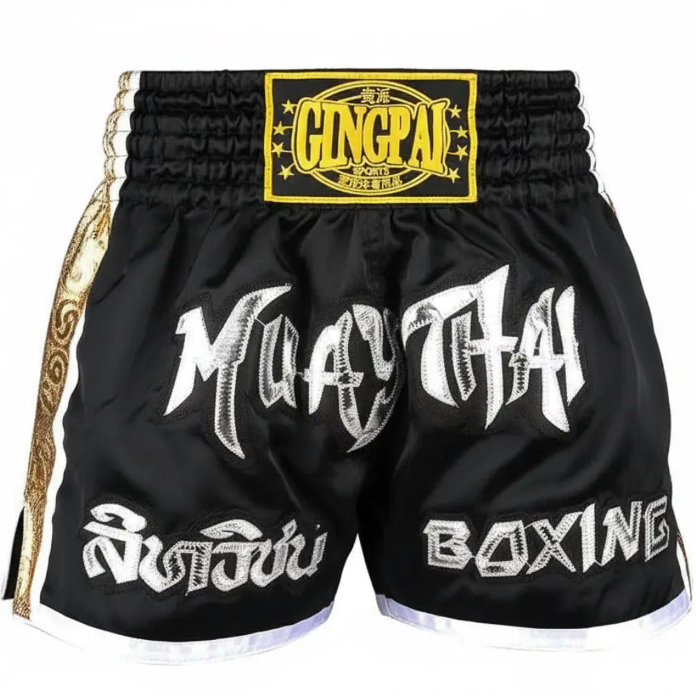 Black Muay Thai boxing shorts with white and silver graphic lettering, a yellow and black Glingpai waist patch, and gold side trim.