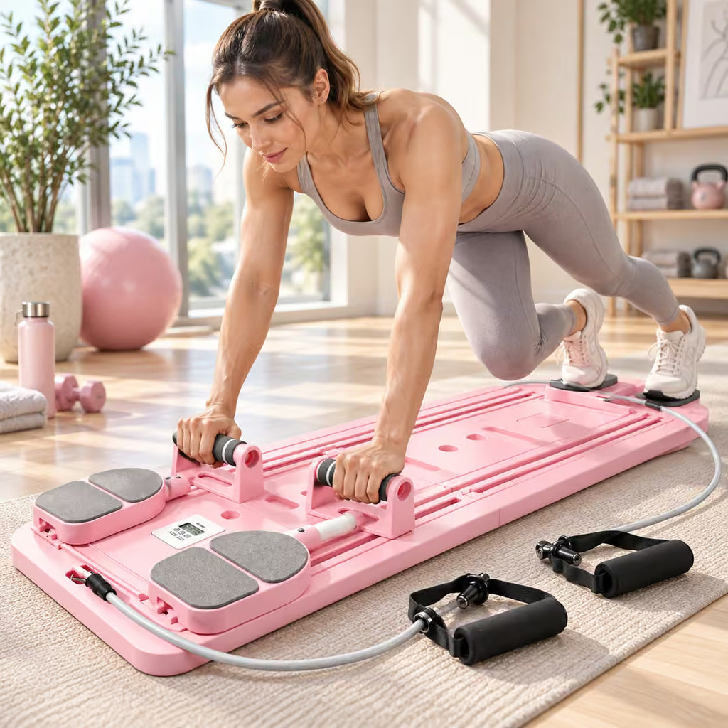 A woman in a gray sports bra and leggings performs a plank-style exercise on a pink abdominal trainer pad with resistance handles and a connected resistance band in a bright, modern home gym.