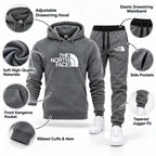A dark gray The North Face hoodie and matching jogger pants shown on a white background with callout circles highlighting features such as the adjustable drawstring hood, soft high-quality materials, kangaroo pocket, ribbed cuffs and hem, elastic drawstring waistband, side pockets, and tapered jogger fit.