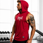 A man in a gym wearing a red sleeveless hooded tank top with the Everlast logo on the chest, paired with black shorts.