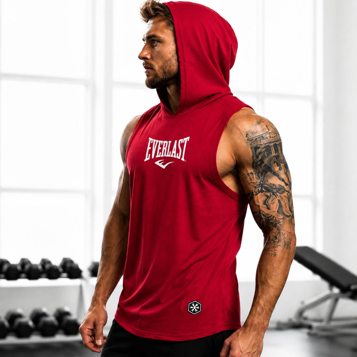 A man in a gym wearing a red sleeveless hooded tank top with the Everlast logo on the chest, paired with black shorts.