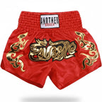 Red Muay Thai boxing shorts with gold and black embroidered graphics, featuring a white waistband label that reads 'ANOTHER BOXER'.