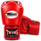 A pair of red leather boxing gloves with white and black branding. One glove is upright, showing the Twins Spirit logo on the knuckle area and a Twins brand wrap around the wrist.