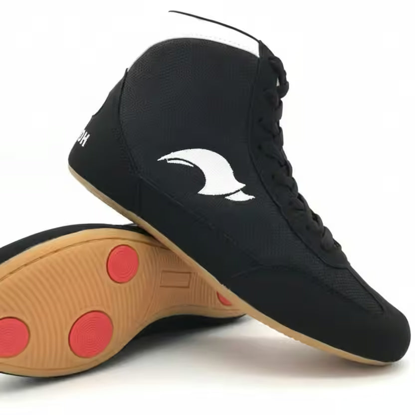A pair of black high-top athletic sneakers shown on a white background, with one shoe standing upright and the other lying on its side to display the tan outsole with red circular pads.