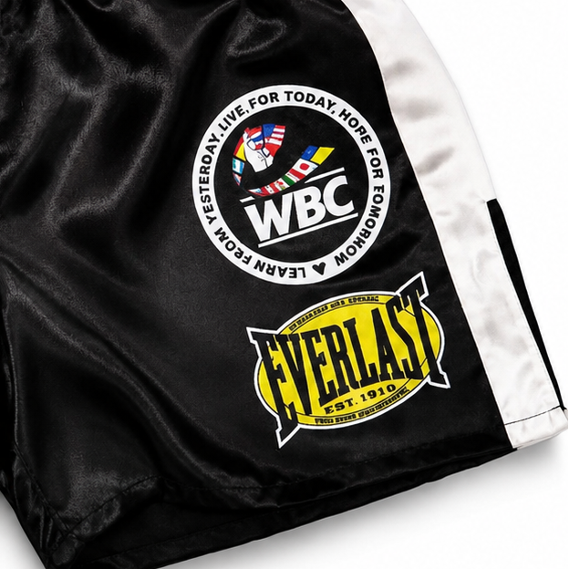 Black and white boxing shorts with multiple brand patches, including DAZN, WBC, Golden Boy, and Everlast, on a white background.